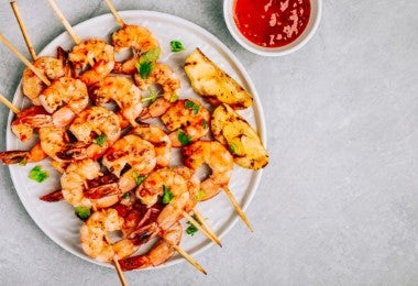 Brocheta de gambas y camarones con salsa de tomate en toma cenital.