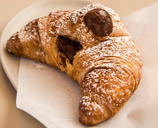 Delicioso croissant relleno de chocolate y espolvoreado con azúcar pastelera, similar al croissant de almendras