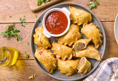 Plato de empanadas con un dip de tomate, un frito similar a los buñuelos de mandioca.