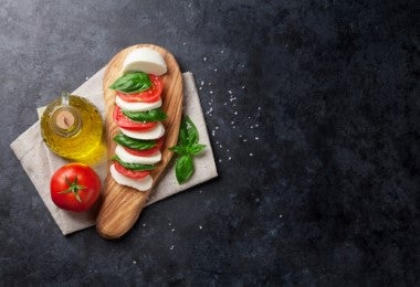 Ensalada caprese con aceite de oliva y un tomate sobre una tabla.