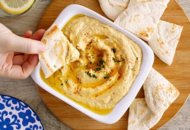 Recipiente lleno de hummus con pan pita, para acompañar la hamburguesa falafel