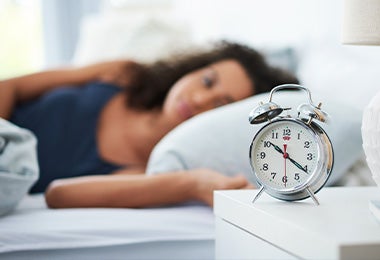 Mujer durmiendo y un reloj de alarma a su lado, lo que regula sus horas de sueño y le da un buen descanso