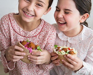 Niñas degustando alegremente pitas rellenas de falafel, un pan árabe muy similar a la focaccia italiana