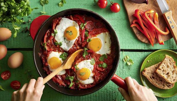 Huevos shakshuka con hierbas, salsa de tomate, pan y pimentón picado en toma cenital